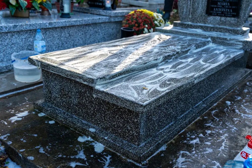 Preparing a grave for All Saints' Day celebrated on November 1st, a woman cleans and washes a marble tomb using a special cleaning solution, brush, cloth, and water. The tomb is clean.