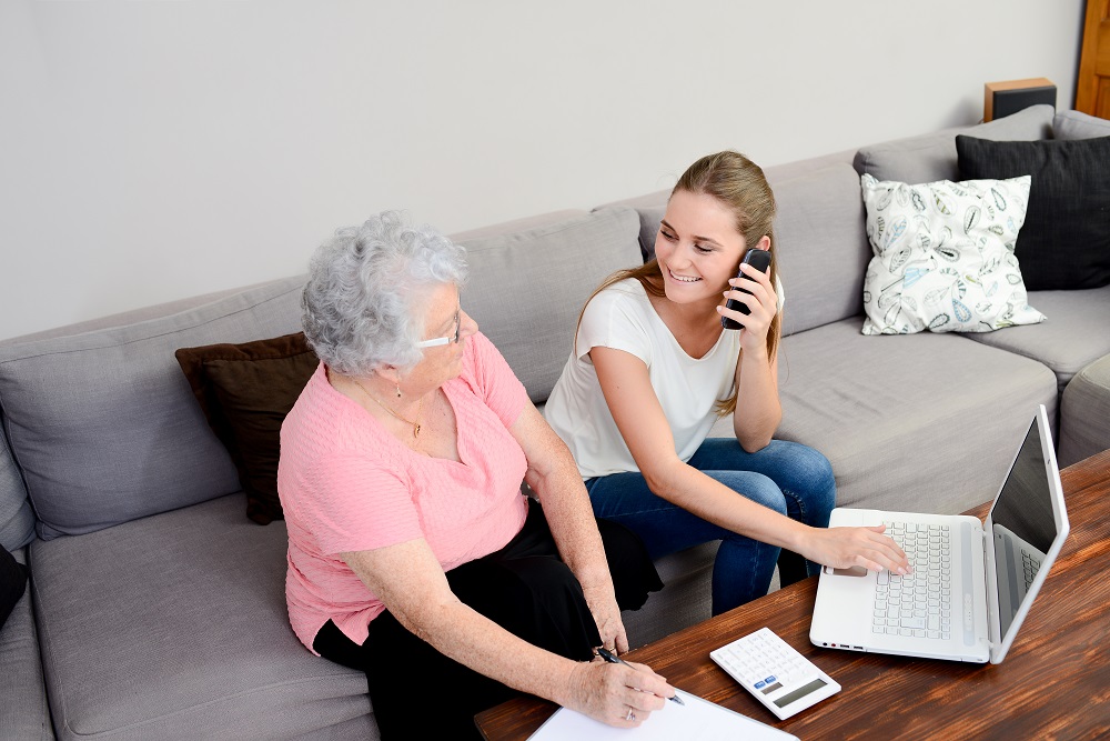 cheerful young woman helping old person doing paperwork and telephone call